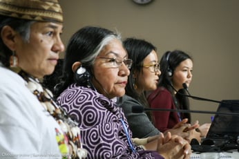 a group of women sit in front of microphones, looking onwards into the crowd