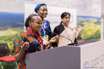 a woman stands at a podium, addresing a crowd