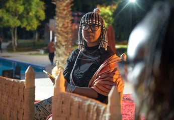 a woman with an intricate hairstyle sits speaking with a group at night